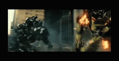 Two Transformers Are Fighting Each Other In A City While A Car Is On Fire . GIF