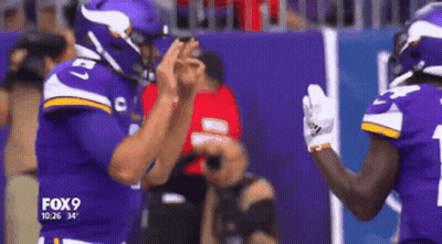 Two Vikings Football Players Are High Fiving Each Other On The Field GIF