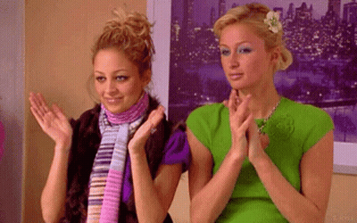 two women are clapping their hands in front of a picture of a city at night .