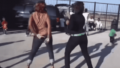 two women are dancing in a parking lot in front of a suv