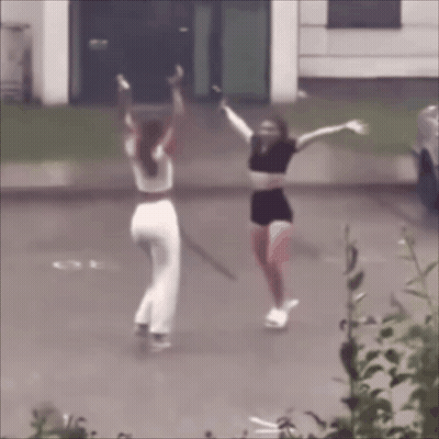 Two Women Are Dancing In A Parking Lot With Their Arms Outstretched GIF