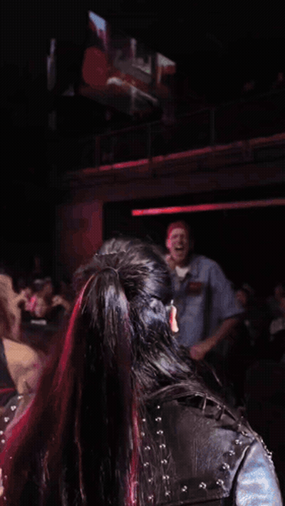 Two Women Are Dancing In Front Of A Crowd In A Dark Room With A Large Screen Behind Them GIF
