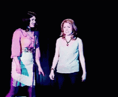 Two Women Are Dancing In Front Of A Microphone And One Has Her Arm In The Air GIF