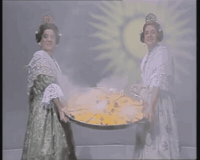Two Women Are Holding A Large Tray Of Food In Front Of A Sun GIF