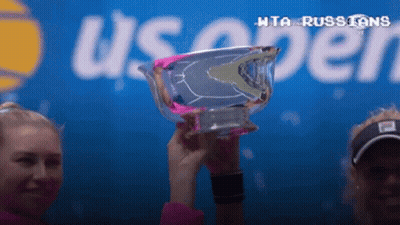 Two Women Are Holding A Trophy In Front Of A Sign That Says Us Open GIF