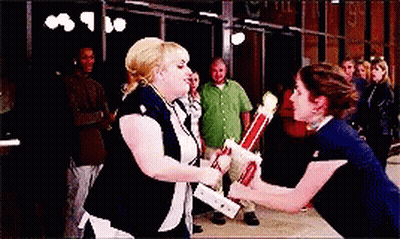 Two Women Are Holding Trophies In Front Of A Group Of People GIF