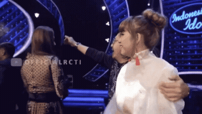 Two Women Are Hugging In Front Of An Indonesia Idol Sign GIF