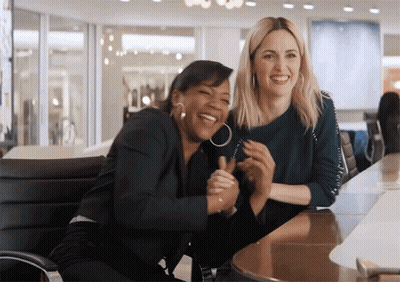 Two Women Are Laughing And Hugging Each Other While Sitting At A Table GIF