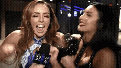 Two Women Are Laughing While Holding A Microphone With The W Logo On It GIF