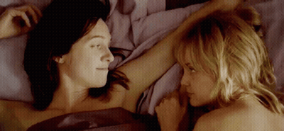 Two Women Are Laying In Bed Looking At Each Other And Touching Each Other 'S Arms . GIF