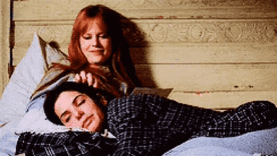 Two Women Are Laying On A Bed One Is Reading A Book GIF