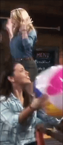 Two Women Are Playing With A Beach Ball In Front Of A Menu GIF