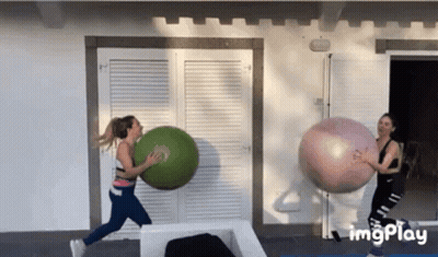 Two Women Are Playing With Giant Exercise Balls In Front Of A Building . GIF