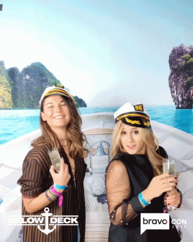 Two Women Are Posing For A Photo In Front Of A Bravo Con Poster GIF