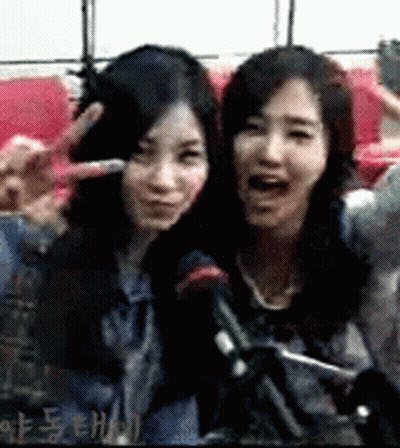 Two Women Are Posing For A Picture And One Is Making A Peace Sign GIF