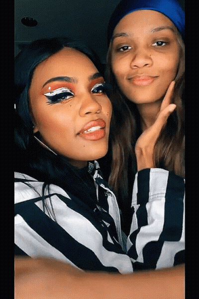 Two Women Are Posing For A Picture With One Wearing A Blue Hat GIF