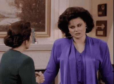 Two Women Are Shaking Hands In A Living Room . GIF