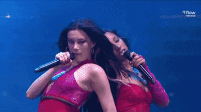 Two Women Are Singing Into Microphones On A Stage With Samsung In The Background GIF