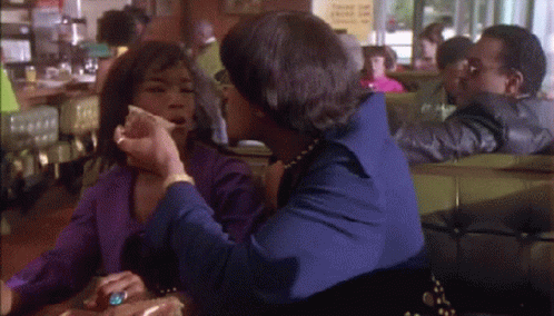 Two Women Are Sitting At A Table In A Diner Talking GIF