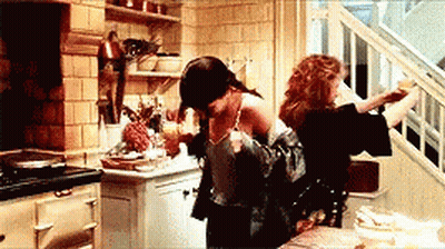 Two Women Are Sitting At A Table In A Kitchen Looking Out A Window . GIF