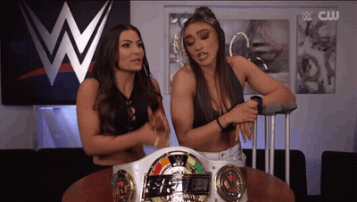 Two Women Are Sitting At A Table In Front Of A Wwe Sign GIF