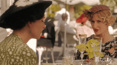 Two Women Are Sitting At A Table With Netflix Written On The Bottom GIF