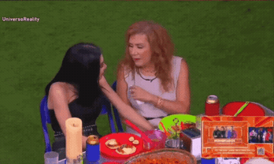 Two Women Are Sitting At A Table With Plates Of Food And The Word Universoreality On The Bottom Right GIF
