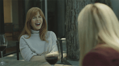 Two Women Are Sitting At A Table With Wine Glasses And One Is Laughing GIF