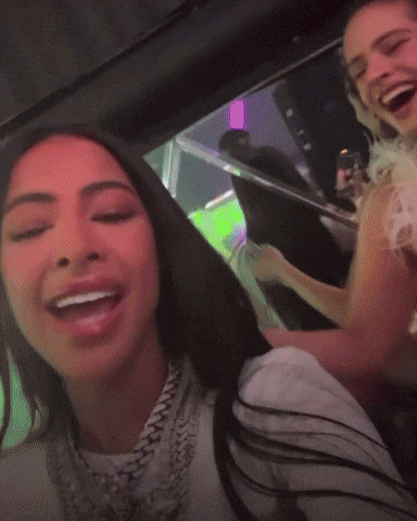 Two Women Are Sitting In A Car And One Is Wearing A White Shirt With A Chain Around Her Neck GIF