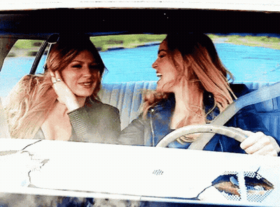 Two Women Are Sitting In A Car Laughing And Talking GIF