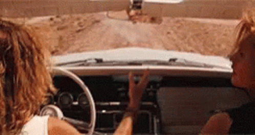 Two Women Are Sitting In A Car On A Dirt Road . GIF
