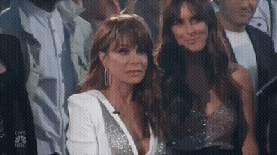 Two Women Are Sitting In A Crowd And One Is Wearing A White Jacket . GIF