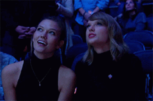Two Women Are Sitting In A Stadium Looking Up At The Sky . GIF