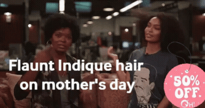 Two Women Are Sitting In Front Of A Sign That Says Flaunt Indicue Hair On Mother 'S Day GIF
