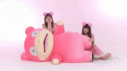 Two Women Are Sitting Next To A Pink Stuffed Animal . GIF