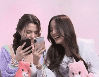 Two Women Are Sitting Next To Each Other And Looking At Their Phones . GIF