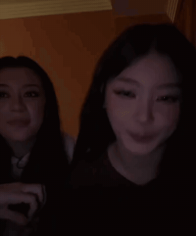 Two Women Are Sitting Next To Each Other In A Dark Room And Smiling . GIF