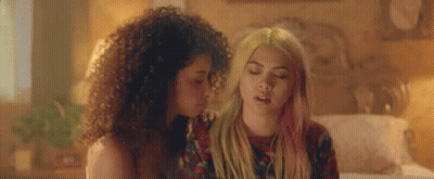 Two Women Are Sitting Next To Each Other On A Bed . One Of The Women Has Pink Hair . GIF