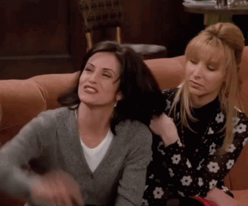 Two Women Are Sitting Next To Each Other On A Couch And One Is Holding The Other 'S Hair . GIF