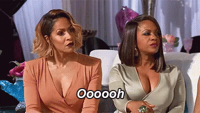 Two Women Are Sitting Next To Each Other On A Couch And One Of Them Is Wearing A Plunging Neckline Dress . GIF