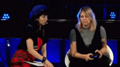Two Women Are Sitting Next To Each Other On A Stage And One Of Them Is Holding A Video Game Controller . GIF