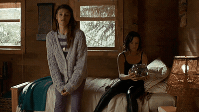 Two Women Are Sitting On A Bed In A Cabin Holding A Jar . GIF