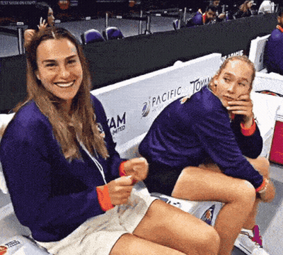 Two Women Are Sitting On A Bench With Pacific Tommy Written On The Wall Behind Them GIF