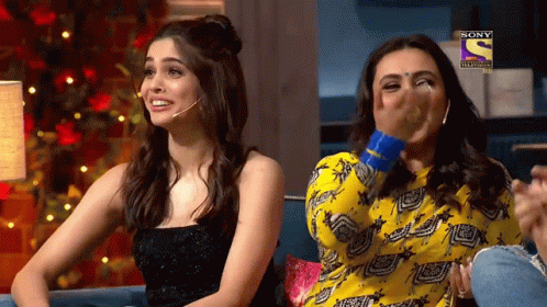Two Women Are Sitting On A Couch And One Of Them Is Covering Her Mouth With Her Hand While The Other Is Laughing .. GIF