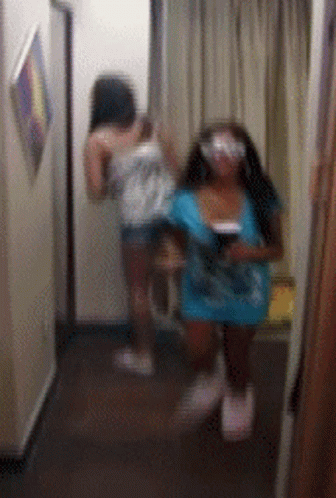 Two Women Are Standing In A Hallway Looking At Each Other GIF