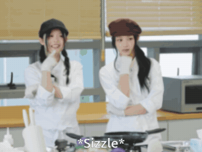 Two Women Are Standing In A Kitchen And The Word Sizzle Is On The Bottom Left GIF