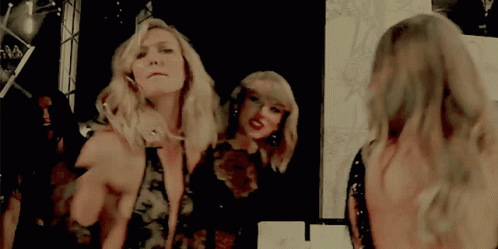 Two Women Are Standing In Front Of A Mirror Looking At Their Reflection GIF