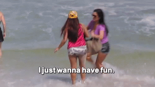 Two Women Are Standing In The Ocean With The Words `` I Just Wanna Have Fun '' Above Them . GIF