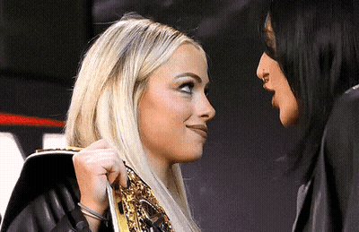 Two Women Are Standing Next To Each Other And Looking At Each Other . One Of The Women Is Wearing A Wrestling Belt . GIF