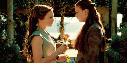 Two Women Are Standing Next To Each Other And Looking At Each Other . One Woman Is Holding A Flower . GIF